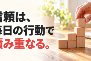 朝の光が差す机で木のブロックを積み重ねる手元と、「信頼は、毎日の行動で積み重なる。」の文字。